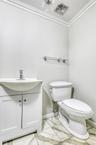 Bathroom with toilet, marble look tiles, vanity, baseboards, and crown molding