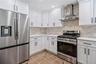 Modern kitchen featuring white shaker cabinetry with black hardware, stainless steel appliances, light-toned stone backsplash, and light-toned counter