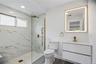 Bathroom en-suite featuring a frameless glass shower enclosure with gold-finish hardware, marble-look tiled walls, pebble shower pan, and a floating v