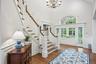 Hardwood flooring, grand staircase with white risers and wood treads, chandelier, double French doors, transom window with arched top