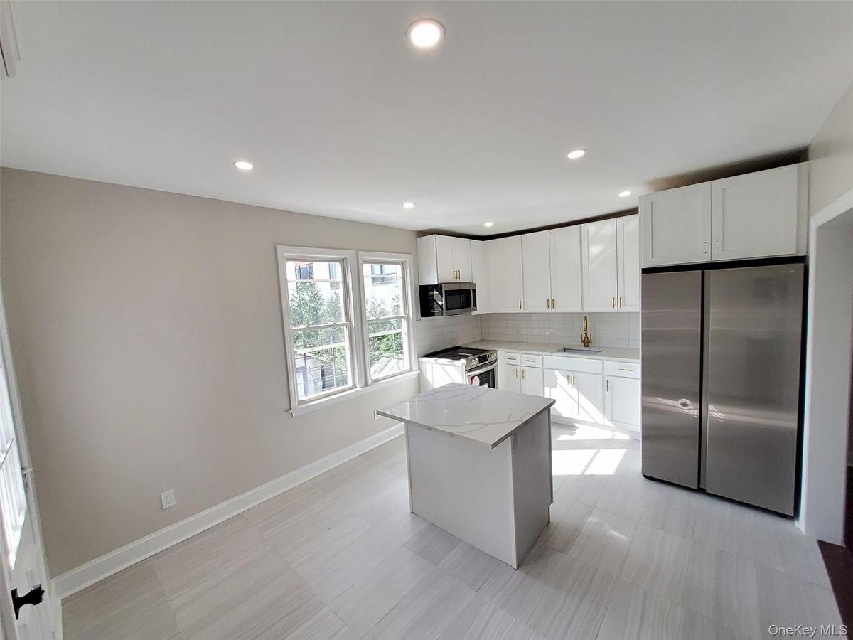 Kitchen featuring a center island, white cabinets, tasteful backsplash, light stone counters, and stainless steel appliances