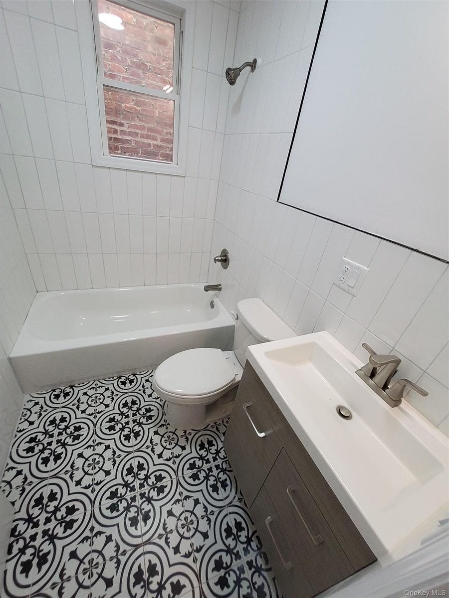 Full bathroom with tile patterned floors, vanity, tile walls, toilet, and tiled shower / bath