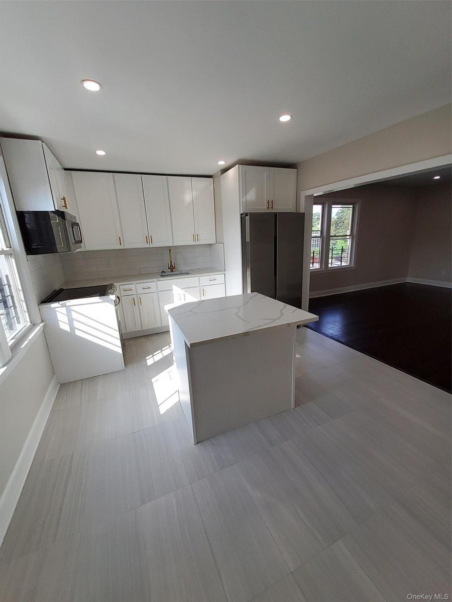 Kitchen featuring light stone countertops, refrigerator, sink, white cabinets, and a kitchen island