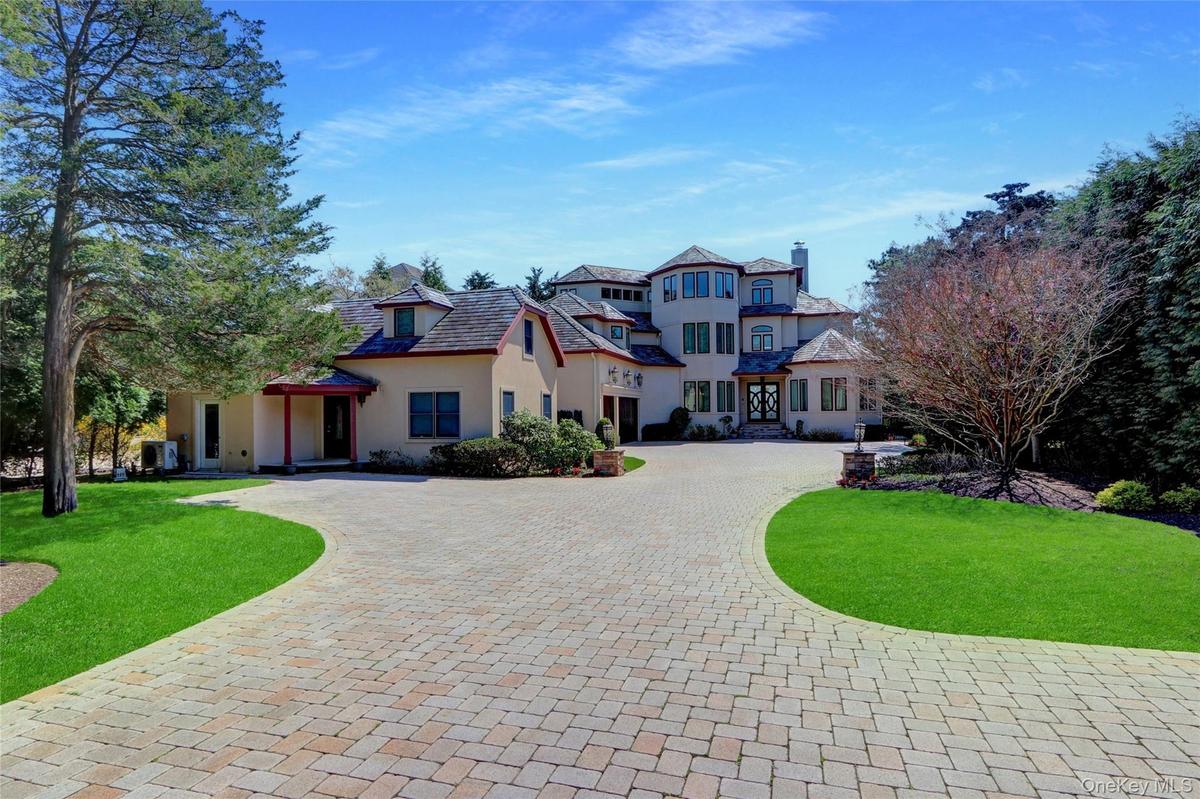 View of front of home featuring a front yard, stucco siding, curved driveway, and a chimney