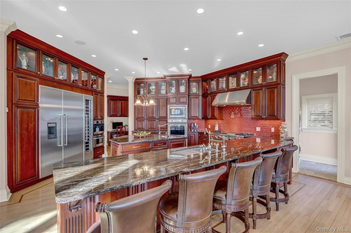 Kitchen featuring under cabinet range hood, built in appliances, dark brown cabinets, a sink, and a center island with sink