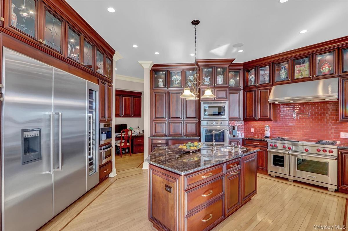 Kitchen with reddish brown cabinets, decorative light fixtures, under cabinet range hood, built in appliances, and light wood-type flooring