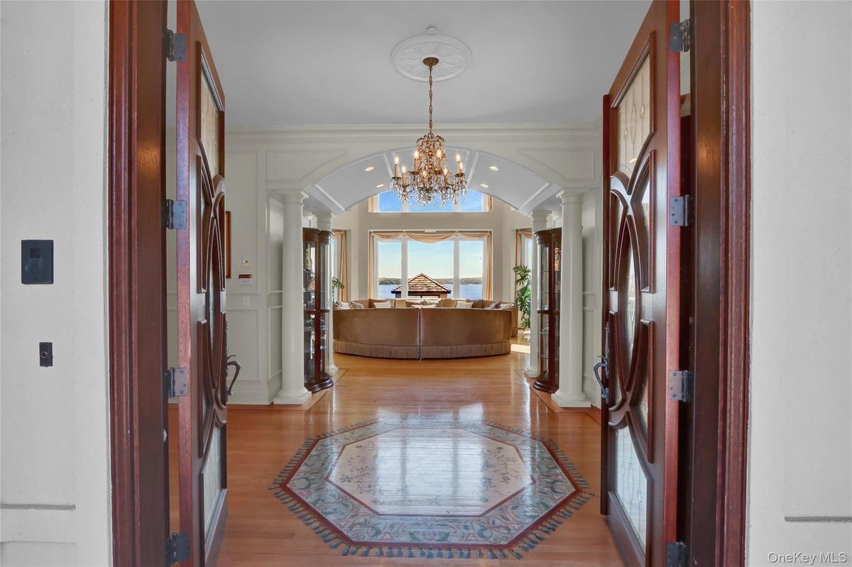 Entryway featuring a notable chandelier, crown molding, light wood-style flooring, ornate columns, and arched walkways