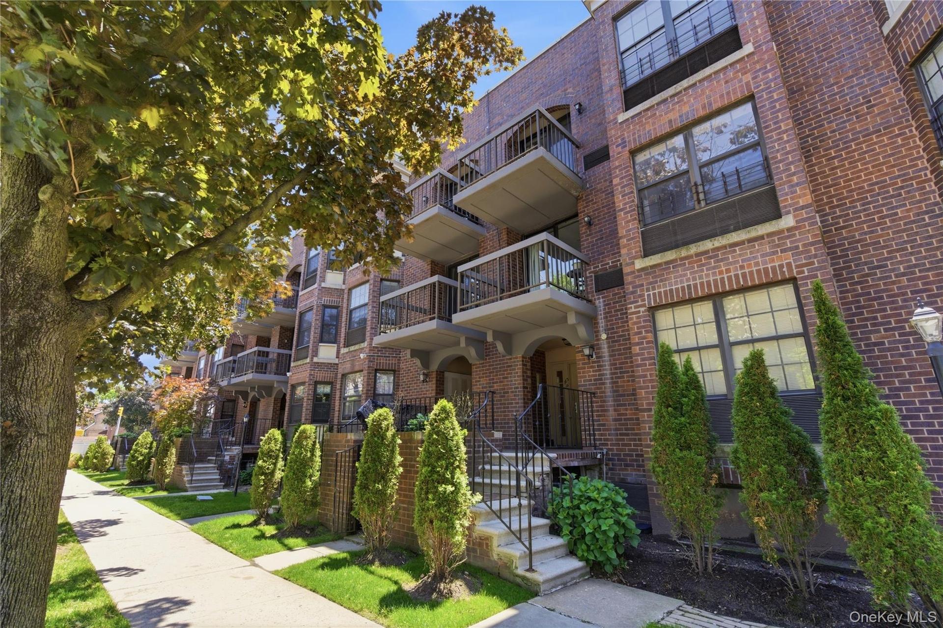 Brick exterior multifamily building featuring multiple balconies, individual ground-level entryways, mature landscaping, and an ornate street lamp