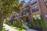 Brick exterior multifamily building featuring multiple balconies, individual ground-level entryways, mature landscaping, and an ornate street lamp