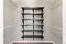 Customizable closet system featuring five dark wood-finish shelves, two hanging rods, light gray wall paint, white baseboards, and wood-finish floorin