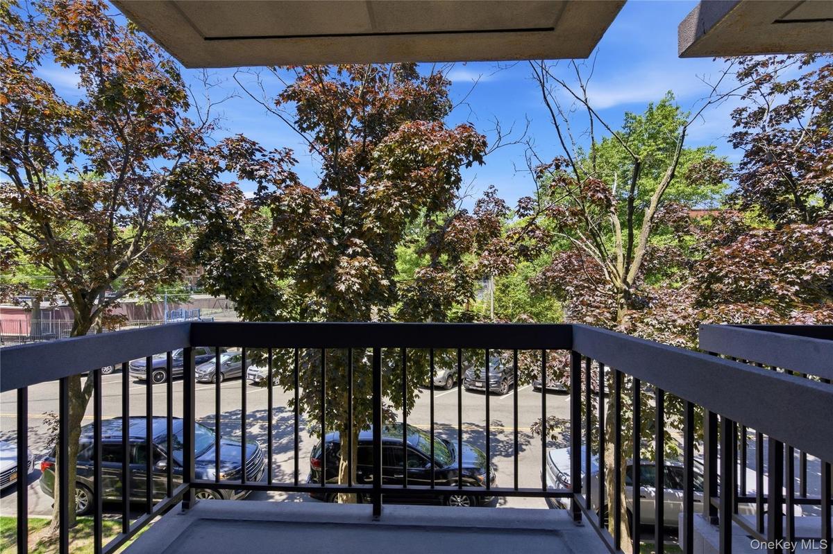Private balcony with dark gray railing and concrete flooring, offering an elevated perspective of the surrounding mature foliage and a paved parking a