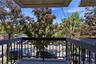 Private balcony with dark gray railing and concrete flooring, offering an elevated perspective of the surrounding mature foliage and a paved parking a