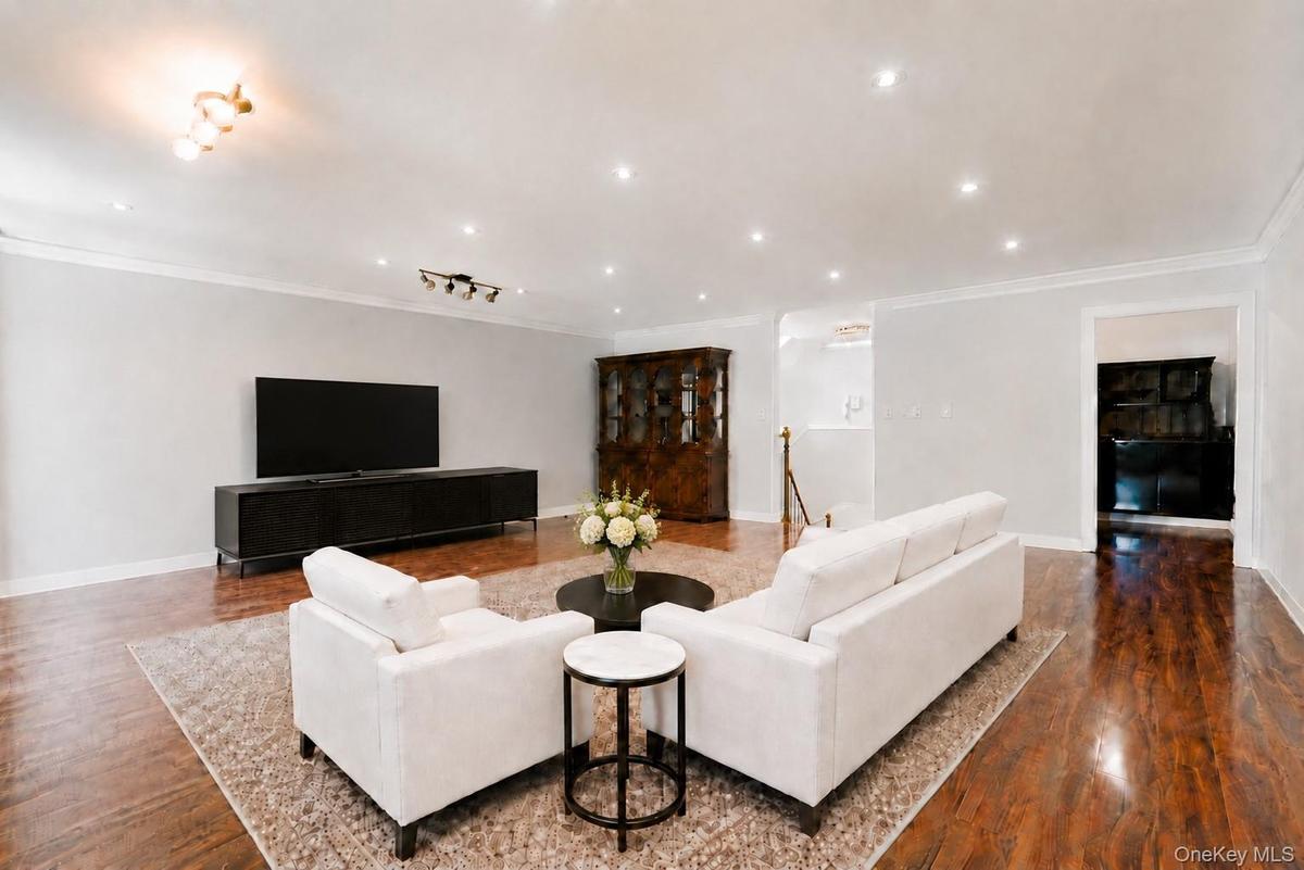 Living area featuring rich wood-finish flooring, recessed lighting, crown molding, and a built-in display cabinet