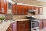 Kitchen with rich wood cabinetry, stainless steel appliances, a corner sink with a black faucet, and patterned mosaic tile backsplash