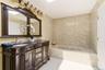 Spacious bathroom featuring a carved dual vanity with undermount sinks, a large framed mirror, and an integrated soaking tub with stone-look surround