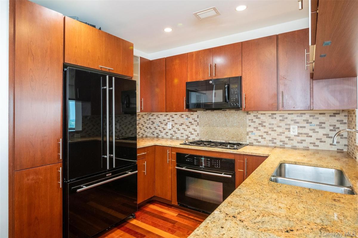 Kitchen with black appliances, wood finished floors, tasteful backsplash, light stone counters, and recessed lighting