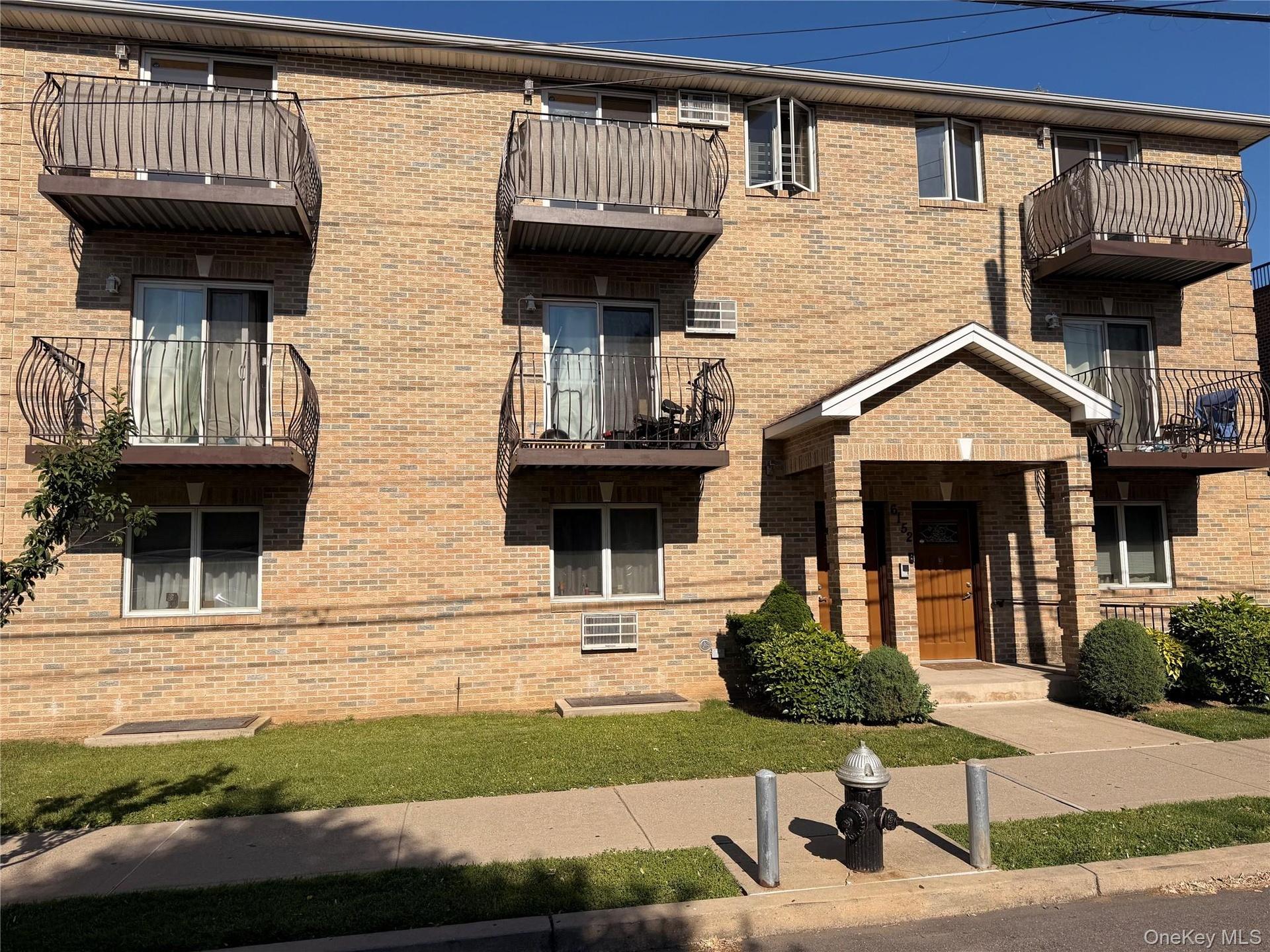 Brick exterior building featuring multiple private balconies with decorative metal railings, a covered entrance with a gabled roofline, and ground-lev