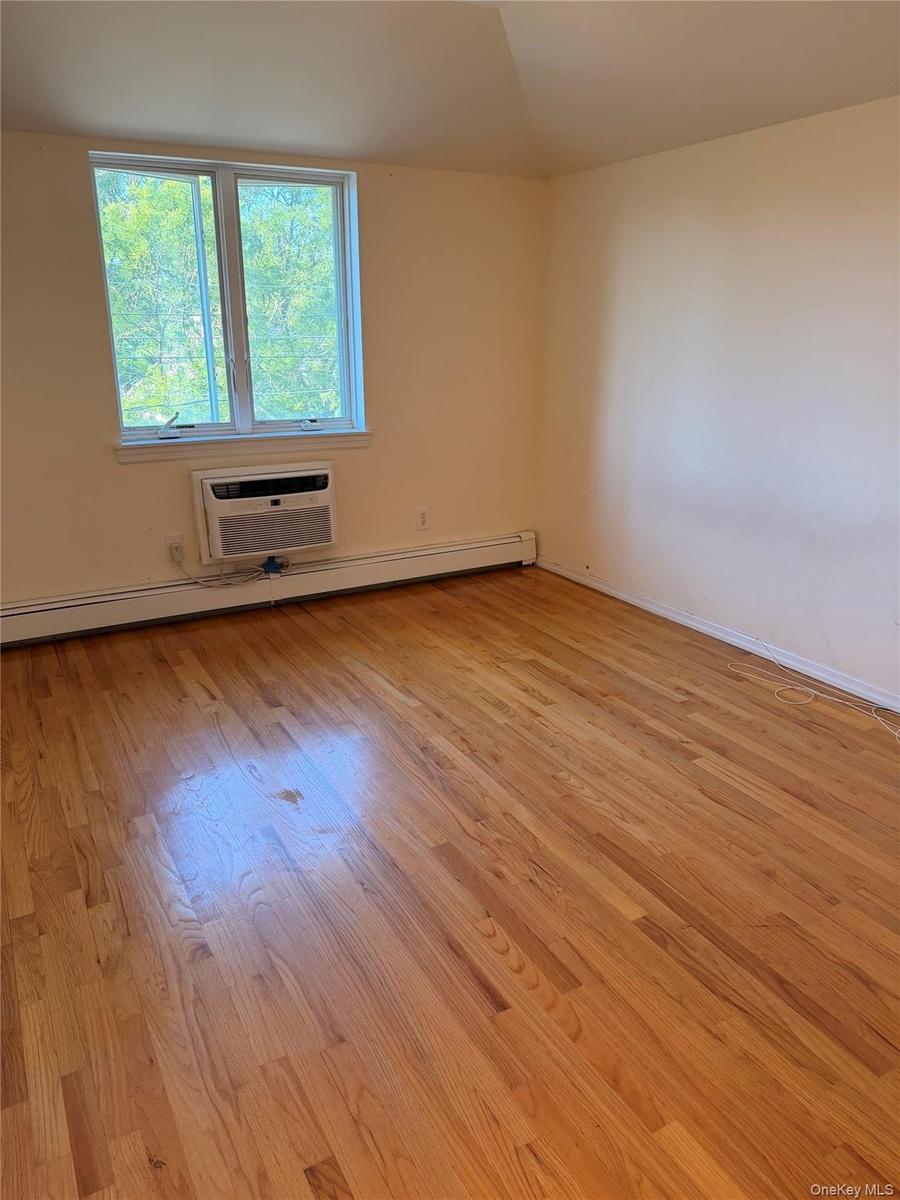 Hardwood flooring throughout featuring light-toned walls, a double window, a window-mounted air conditioning unit, and baseboard heating