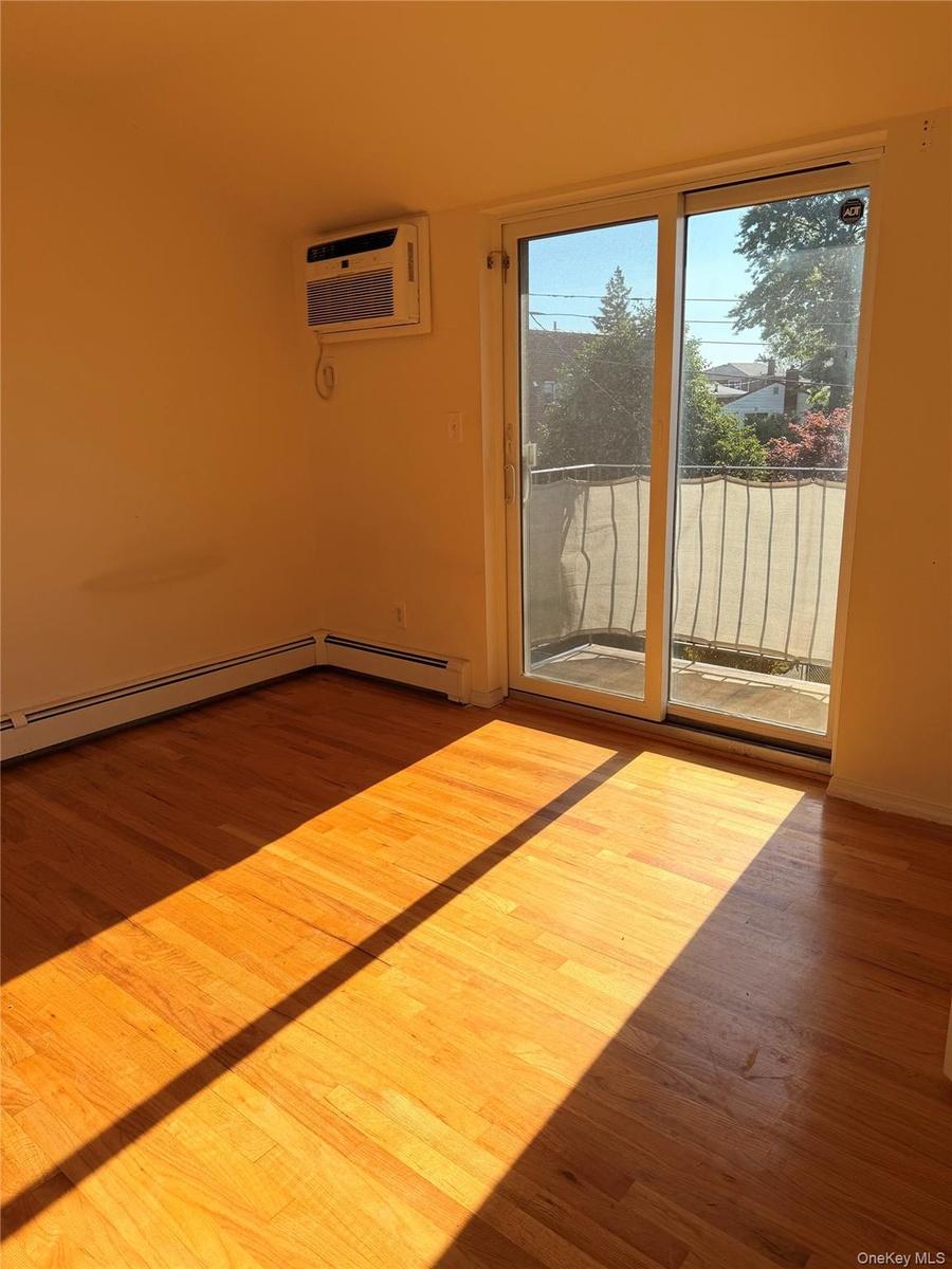 Room featuring wood-finish flooring, white baseboards, and a wall-mounted air conditioning unit