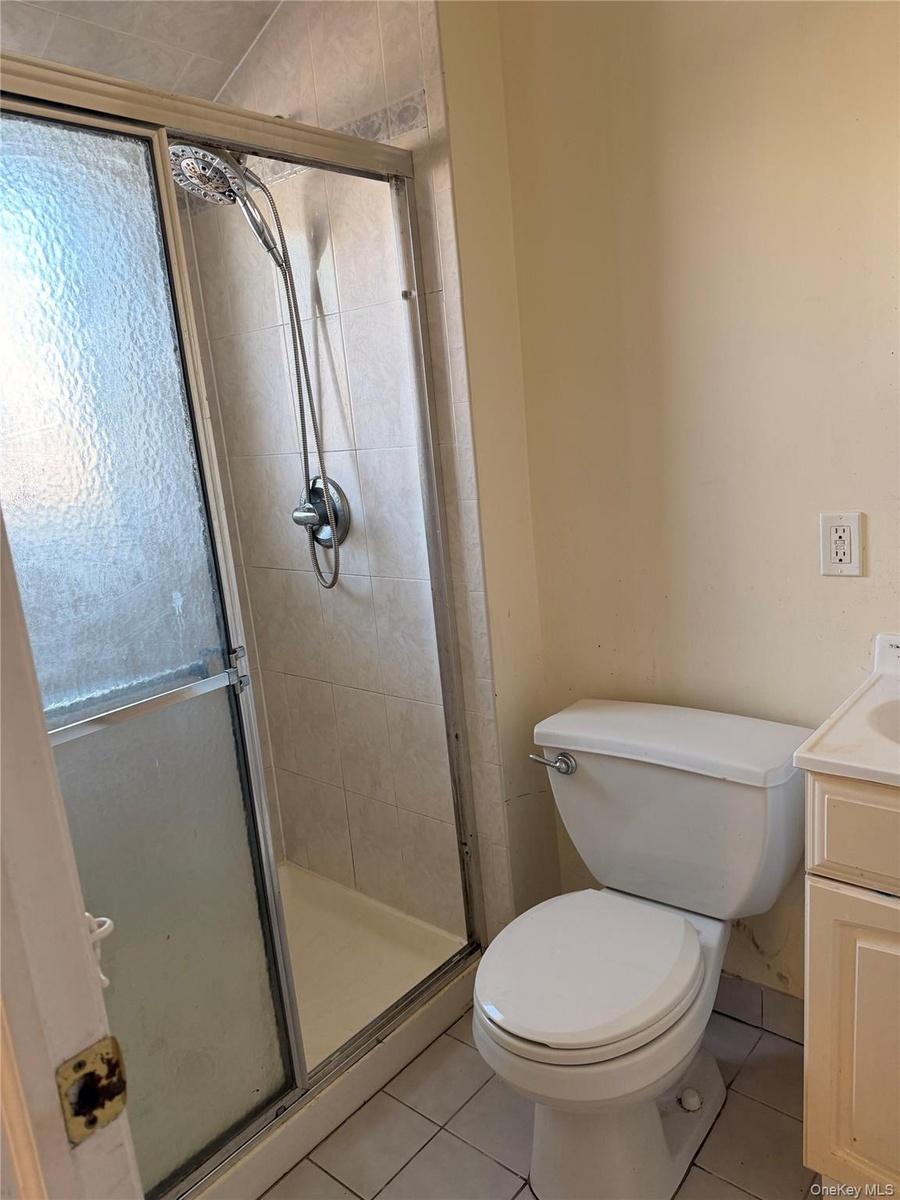 Shower enclosure with textured glass doors, tiled surround, and a detachable showerhead