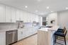 Gourmet kitchen featuring extensive white cabinetry, light-toned stone countertops with matching backsplash, stainless steel appliances, and a central