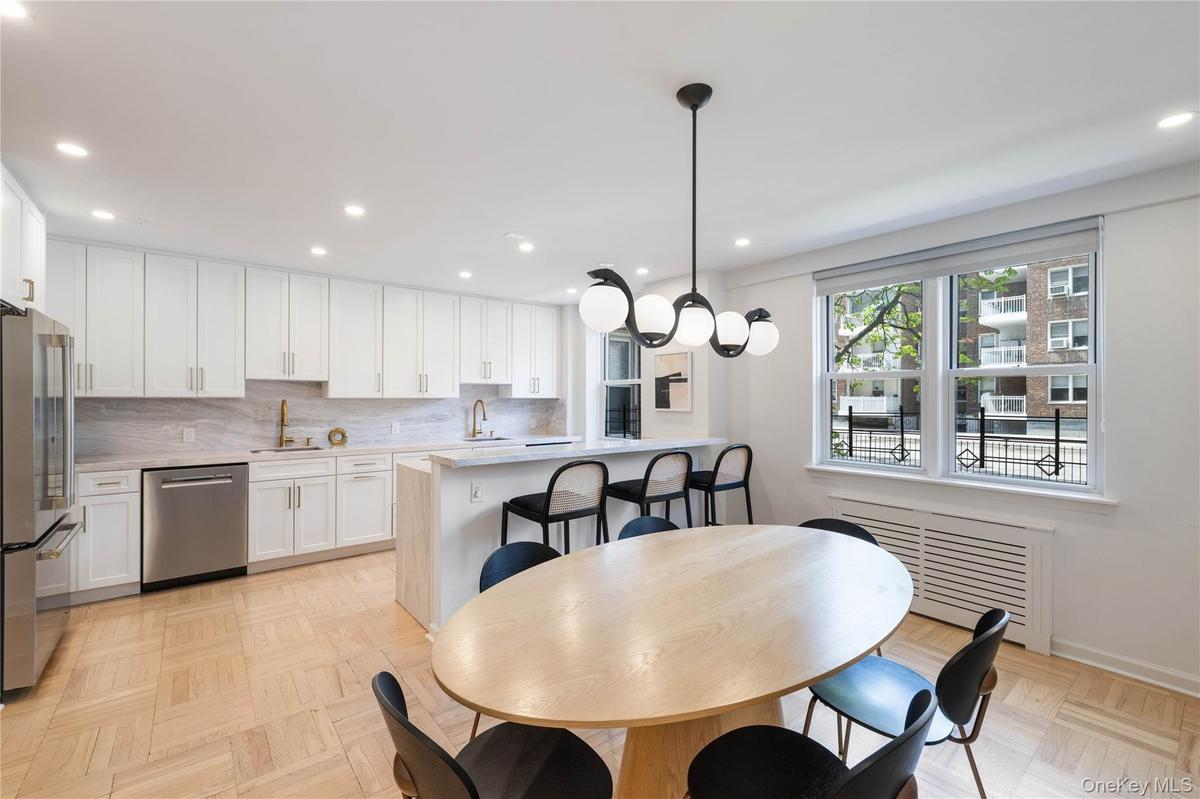 Open-concept kitchen and dining area featuring white shaker cabinetry, stainless steel appliances, a center island with bar seating, and parquet floor