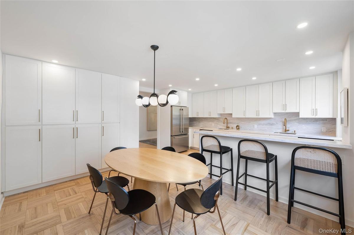 Open-concept kitchen and dining area featuring a full wall of white cabinetry, parquet wood flooring, recessed lighting, and a contemporary spherical 