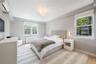 Light-filled bedroom featuring two double-hung windows with Roman shades, a decorative ceiling fixture, and two wall-mounted sconces