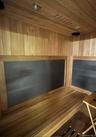 Custom sauna featuring wood paneling throughout, built-in wooden benches, recessed ceiling lighting, and integrated dark panel heating elements