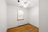 Room featuring wood-finish flooring, a white ceiling fan with integrated lighting, a single window with blinds, and a baseboard heating unit