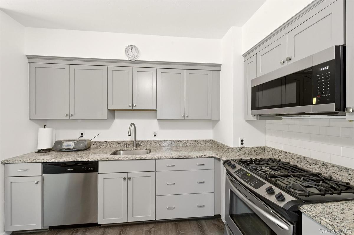 Contemporary kitchen featuring light gray cabinetry, granite countertops, and stainless steel appliances including an over-the-range microwave and a g