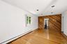 Hardwood flooring throughout, recessed ceiling lighting, baseboard heating, a single window, and a diagonal wood-paneled accent wall with an open door