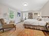 Spacious guest room with ensuite bath room featuring rich wood  flooring, built-in shelving, two large windows, crown molding, and a ceiling-mounted l