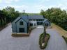 View of front of house with board and batten siding, curved driveway, stone siding, and a view of trees