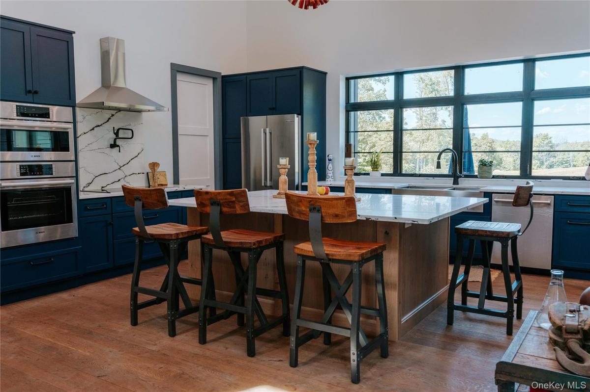Kitchen with tasteful backsplash, blue cabinetry, wall chimney exhaust hood, appliances with stainless steel finishes, and light wood-type flooring