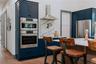 Kitchen featuring blue cabinetry, wall chimney exhaust hood, appliances with stainless steel finishes, and light wood-style floors