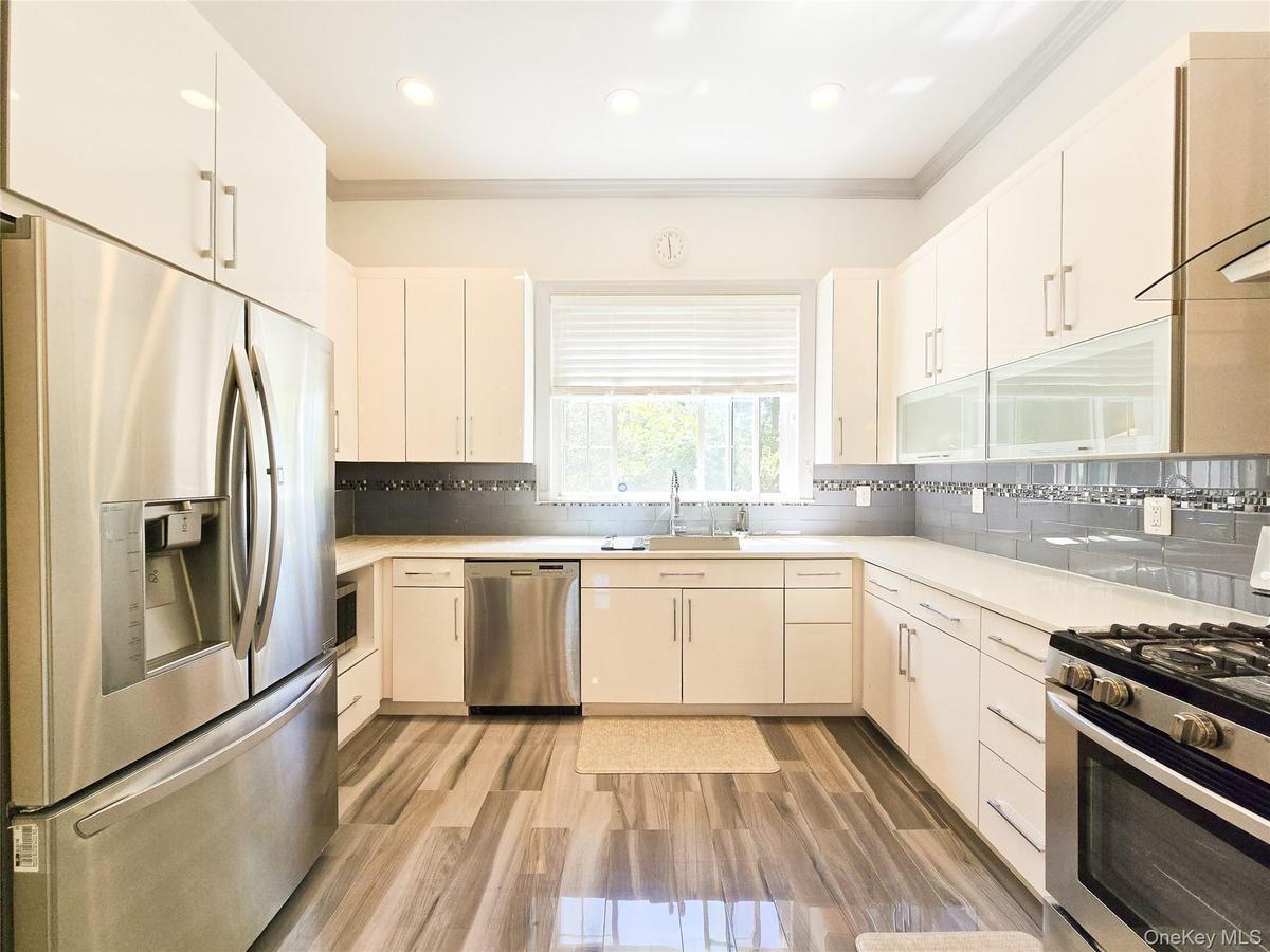 Modern kitchen featuring stainless steel appliances, white cabinetry, wood-finish flooring, and a subway tile backsplash
