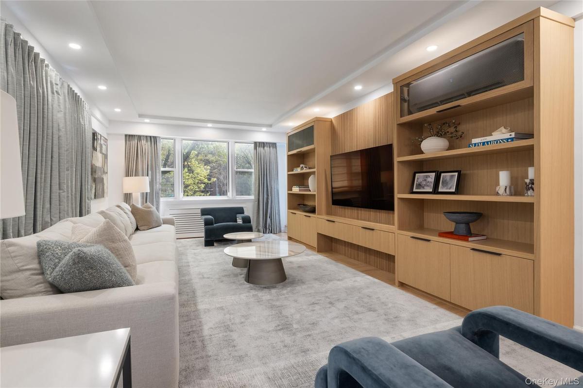Living room featuring custom built-in wood cabinetry and shelving, recessed lighting, expansive windows with custom automated treatments, leading to o