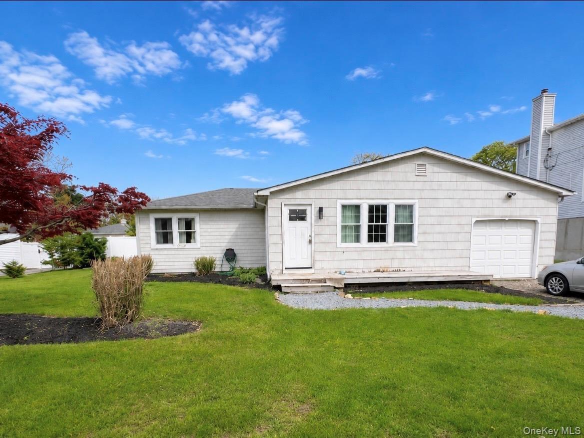 Ranch-style residence featuring light-colored siding, a front entry with a small porch, an attached garage, and a manicured lawn