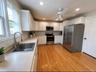Bright kitchen featuring extensive white cabinetry, stainless steel appliances, a large undermount sink, light countertops, and wood-finish flooring