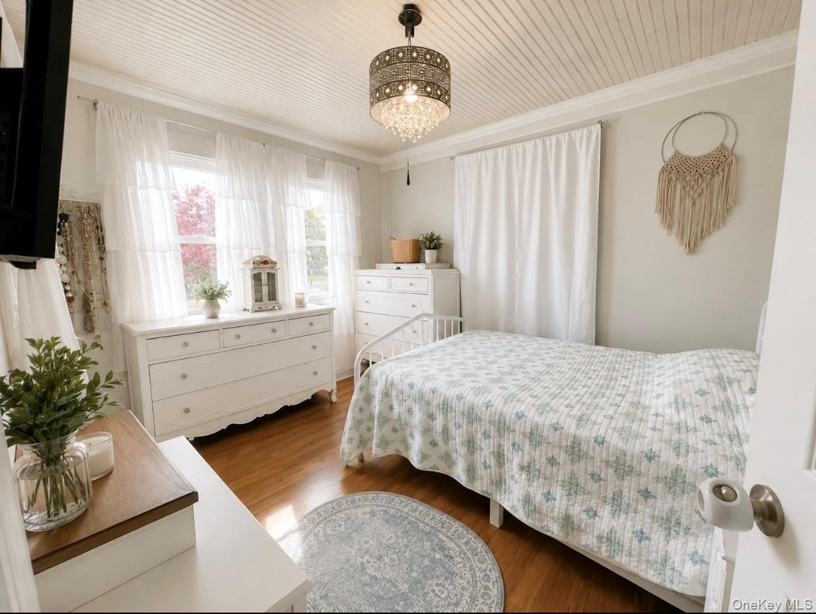 Hardwood flooring, natural light through multiple windows, beadboard ceiling, crown molding, and an ornate ceiling fixture
