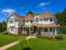 Expansive lawn with a brick paver pathway leading to a two-story residence featuring a covered porch, stone accents, and shake siding