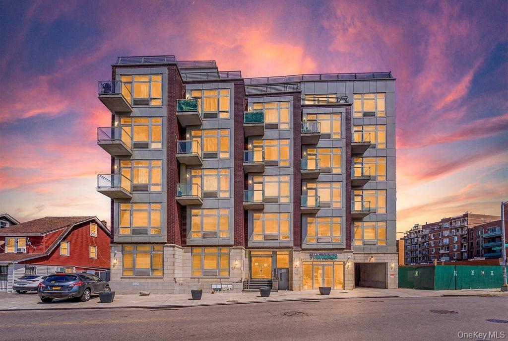 Modern multi-story building featuring a brick and panel facade, individual balconies with glass railings, large windows, an integrated ground-floor en