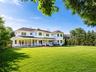 Expansive rear lawn with a two-story residence featuring a full-length covered porch, multiple bay windows, white siding, and a dark shingled roof