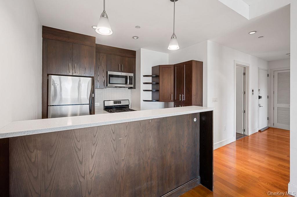 Kitchen featuring dark wood-finish cabinetry, stainless steel appliances, white tile backsplash, and light-colored countertop