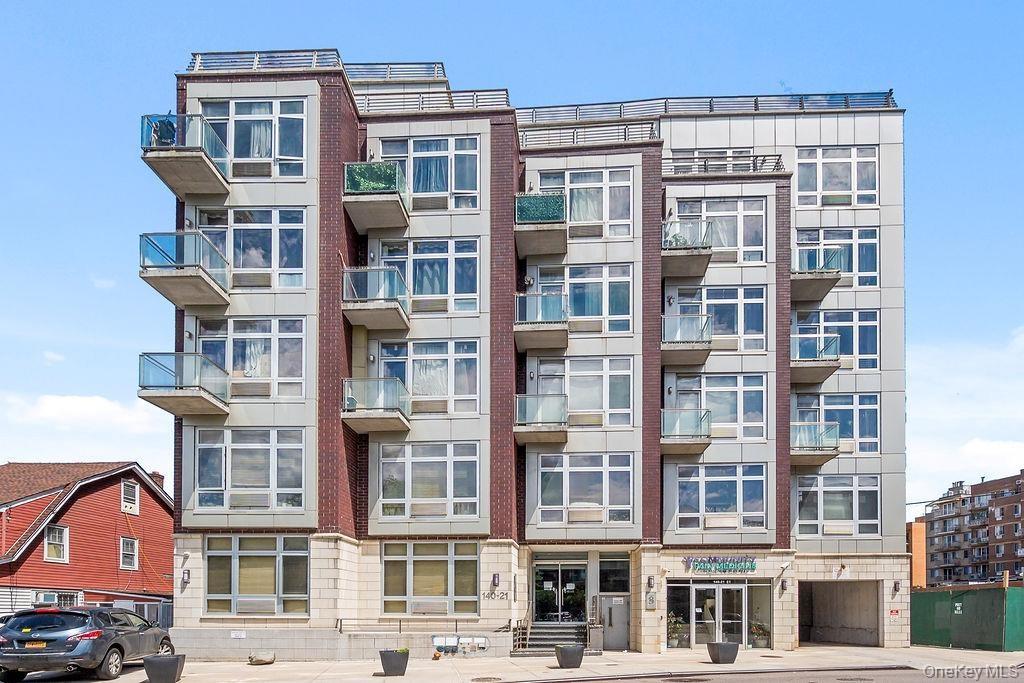 Modern multi-story building featuring brick and panel siding, multiple balconies with glass railings, large windows, and a ground-level entrance with 