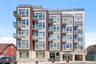 Modern multi-story building featuring brick and panel siding, multiple balconies with glass railings, large windows, and a ground-level entrance with 