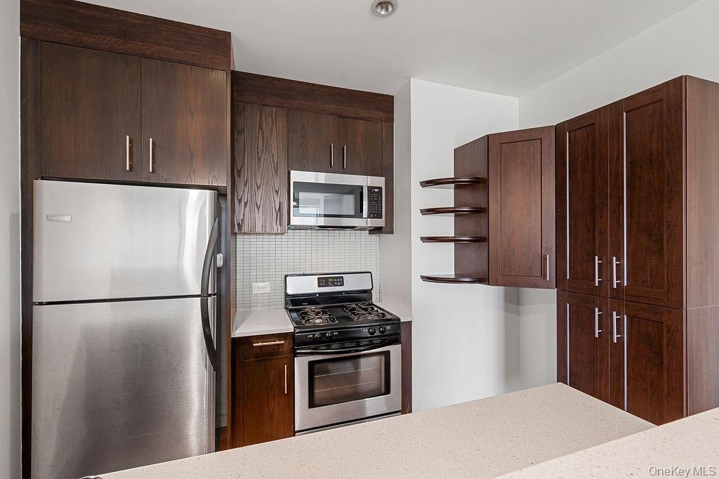 Kitchen featuring dark wood-finish cabinetry, stainless steel appliances, and a mosaic tile backsplash