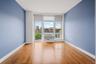 Bright room featuring wood-finish flooring, a large window with white framing, and a wall-mounted air conditioning unit