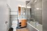 Modern bathroom featuring a soaking tub with glass enclosure, subway tile shower surround, and a wood-finish vanity with an integrated sink
